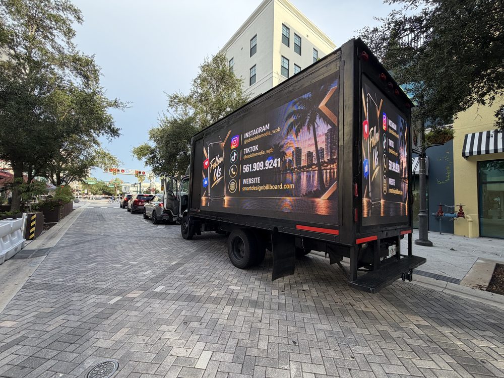 Black box truck with LED screens on the passenger side and rear, parked on a brick street