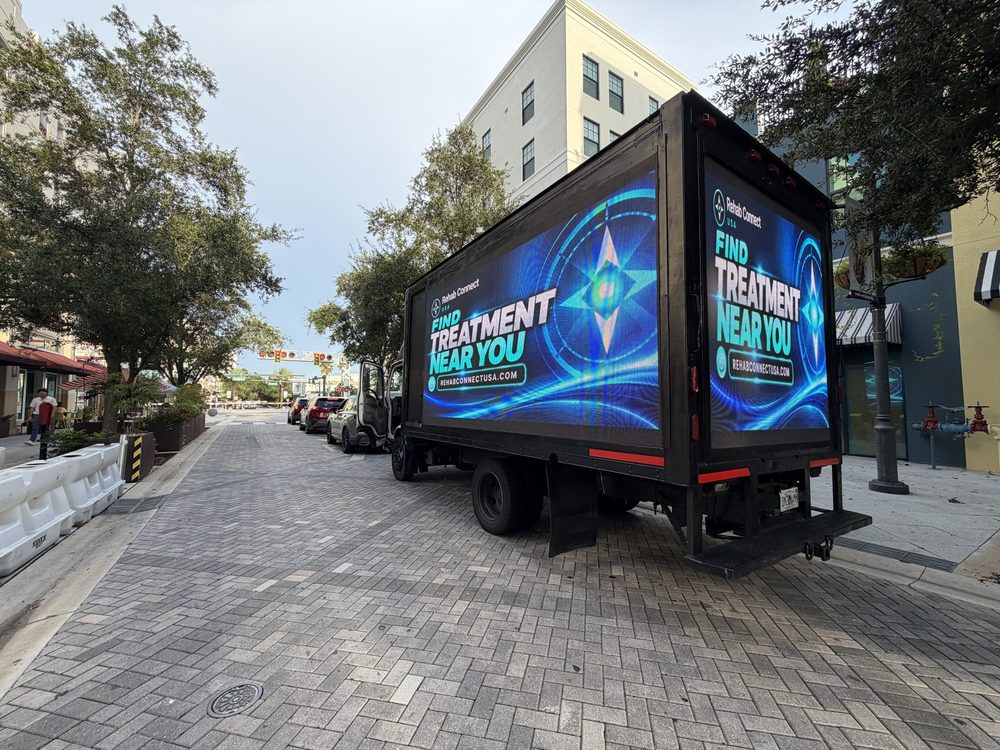 Black box truck with lit LED screens on the passenger side and rear, viewed from behind